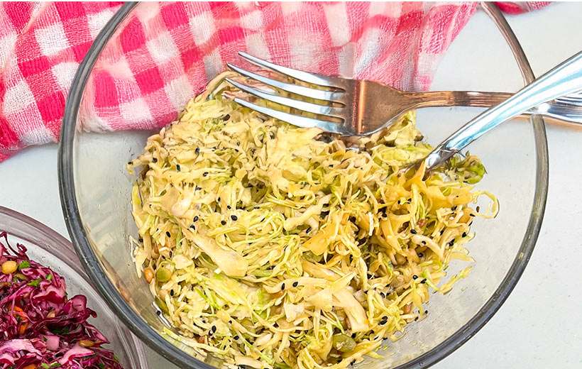 A large bowl with beautiful green cabbage slaw with asian style dressing, mixed with roasted seeds